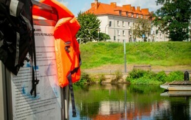 Widok na rzekę i budynek, na pierwszym planie stoi tablica z regulaminem.