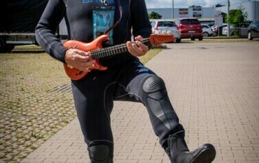 Mężczyzna w okularach przeciwsłonecznych w przebraniu, z gitarą zabawką w rękach.