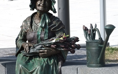 zdjęcie przestawia pomnik starszej kobiety - kwiaciarki z bukietem kwiat&oacute;w