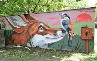 Mural na ścianie garażu przedstawiający głowę lisa, kt&oacute;remu na nosie usiadł ptak.