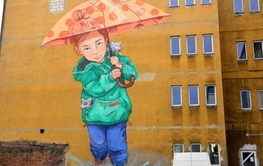 Mural na ścianie budynku przedstawiający dziewczynkę, kt&oacute;ra trzyma nad głową parasolkę. Z kieszeni wystaje jeden szczur, na ramieniu siedzi drugi.