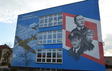 Mural na ścianie budynku przedstawia członk&oacute;w Dywizjonu 303: Jana Zumbacha, Stanisława Skalskiego i Witolda Urbanowicza na tle biało czerwonej szachownicy oraz dwie sylwetki samolotu.