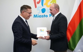 Dw&oacute;ch mężczyzn, jeden wręcza drugiemu czerwoną r&oacute;że i teczkę z logotypem Miasto Piła.