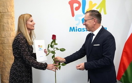 Mężczyzna wręcza kobiecie czerwoną r&oacute;że i teczkę z logotypem Miasto Piła