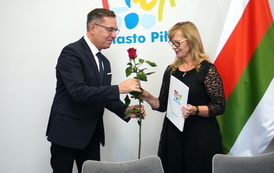 Kobieta trzyma białą teczkę z logotypem Miasto Piła, mężczyzna obok wręcza jej czerwoną r&oacute;żę
