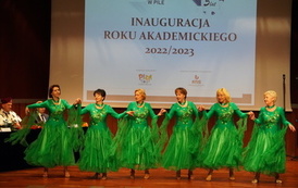 Na scenie grupa starszych kobiet w zielonych sukniach tańczy w rzędzie.
