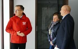 Dw&oacute;ch mężczyzn i kobieta stoją w mieszkaniu. Jeden z mężczyzn ma kurtkę z logotypem Miasto Piła.