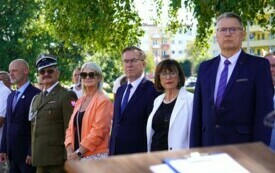 Grupa elegancko ubranych ludzi stojących w rzędzie, wśr&oacute;d nich mundurowi.