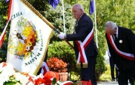 Mężczyzna pochyla sztandar związku pszczelarzy przed pomnikiem, w tle inne poczty sztandarowe.