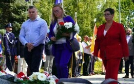 Grupa ludzi składających wiązanki biało-czerwonych kwiat&oacute;w pod pomnikiem. W tle poczty sztandarowe.