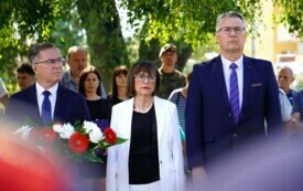 Grupa elegancko ubranych ludzi, kobieta i dw&oacute;ch mężczyzn na pierwszym planie. Jeden z mężczyzn trzyma wieniec biało-czerwonych kwiat&oacute;w.
