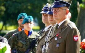 Grupa wojskowych, na pierwszym planie trzech elegancko ubranych mundurowych, w tle kompania honorowa.