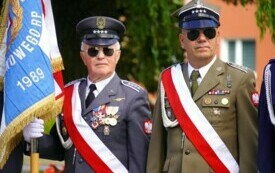 Wojskowi z biało-czerwonymi szarfami i sztandarami.