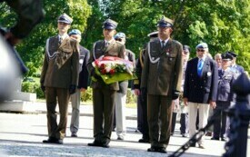 Żołnierze niosący wieniec biało-czerwonych kwiat&oacute;w.