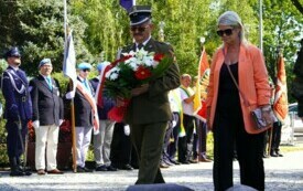 Uroczystości pod pomnikiem, ludzie składający wiązanki biało-czerwonych kwiat&oacute;w. W tle poczty sztandarowe.