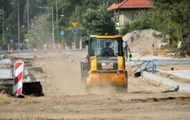 Plac budowy drogi, na pierwszym planie pracująca koparka