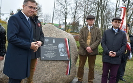 Kilka os&oacute;b odświętnie ubranych, zgromadzonych wok&oacute;ł pomnika - kamienia z tablicą pamiątkową.