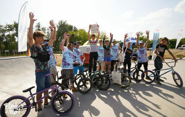 Skateplaza, grupa młodych chłopak&oacute;w z rowerem BMX. Połowa ma jednakowe niebieskie koszulki z napisem &quot;FlowUp&quot;, część z chłopak&oacute;w trzyma ekologiczne torby w rękach.