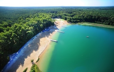 lazurowa tafla jeziora,  plaża i wok&oacute;ł las, zdjęcie robione z lotu ptaka