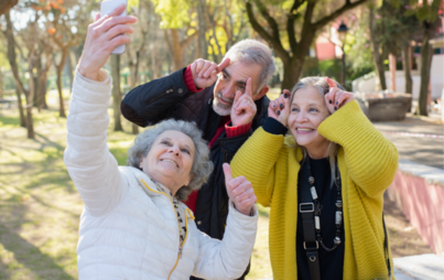 Troje seniorów w parku, pokazują dłońmi rogi i robią zdjęcie