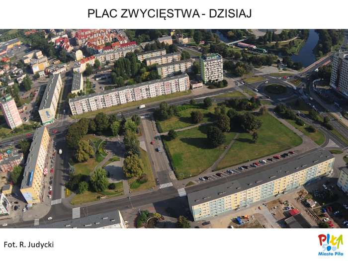 Na zdjęciu miasta wykonanym z lotu ptaka, na pierwszym planie widać plac zieleni, otoczony ulicami i budynkami mieszkalnymi wielorodzinnymi o wysokości 4 i 10 pieter. Po prawej stronie widać rondo, a za nim rzekę.
