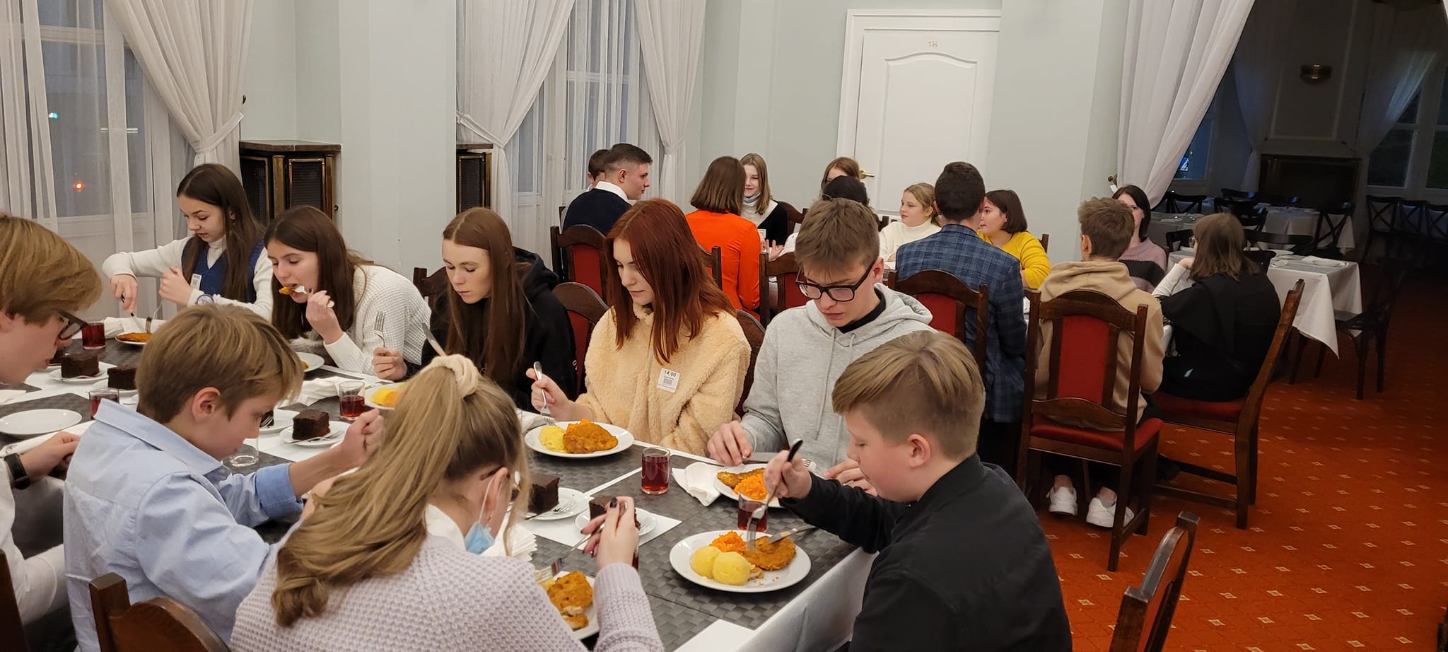 Kilkadziesiąt dzieci i młodych ludzi spożywa posiłek w pomieszczeniu restauracyjnym.