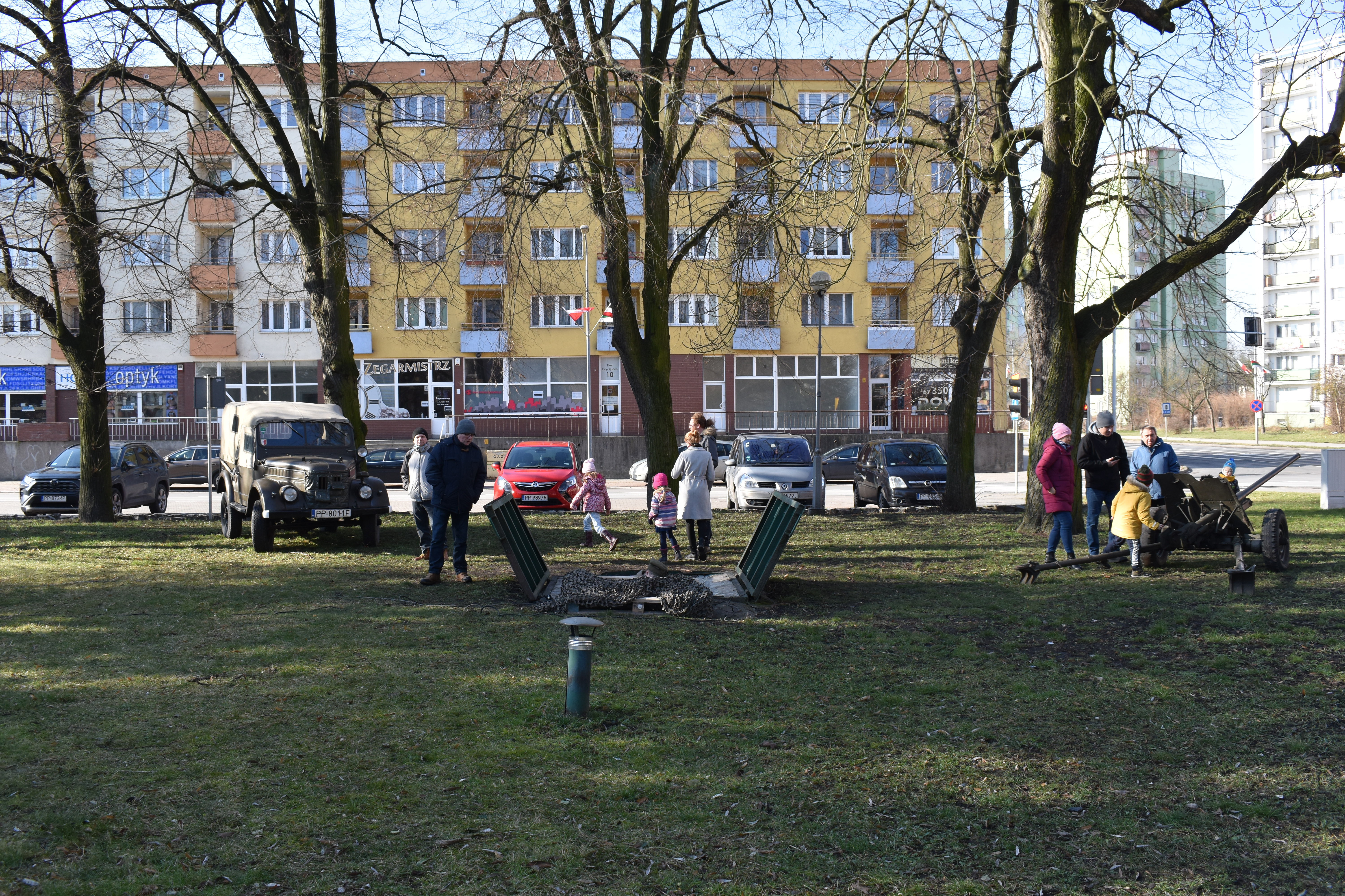 Plac. Trawnik. Ludzie. Samochód terenowy. Armata. Zejście do schronu.