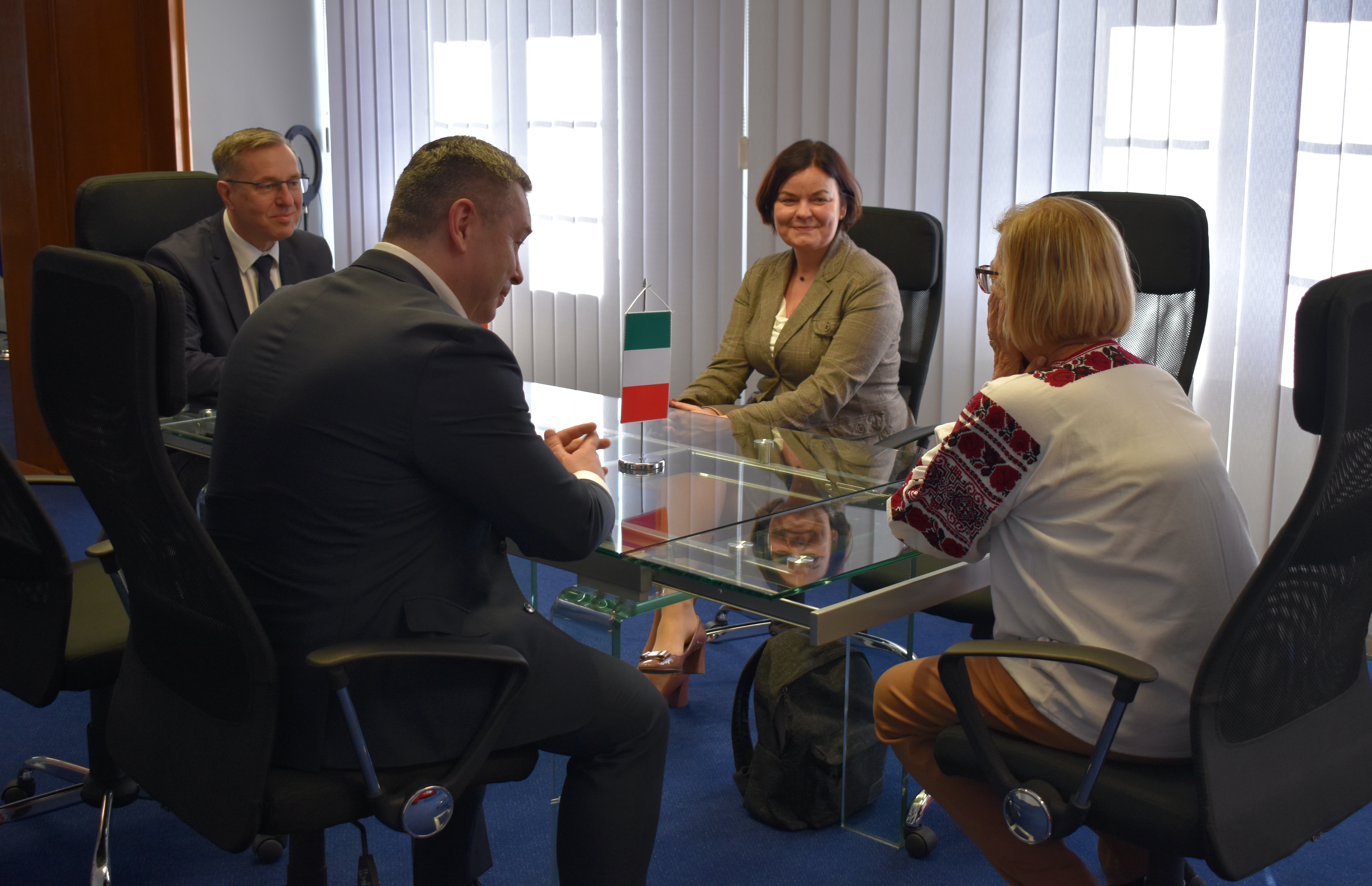 Cztery osoby siedzą przy stole, dwie kobiety i dwóch mężczyzn. Na stole stoi fldgietka Włoch.