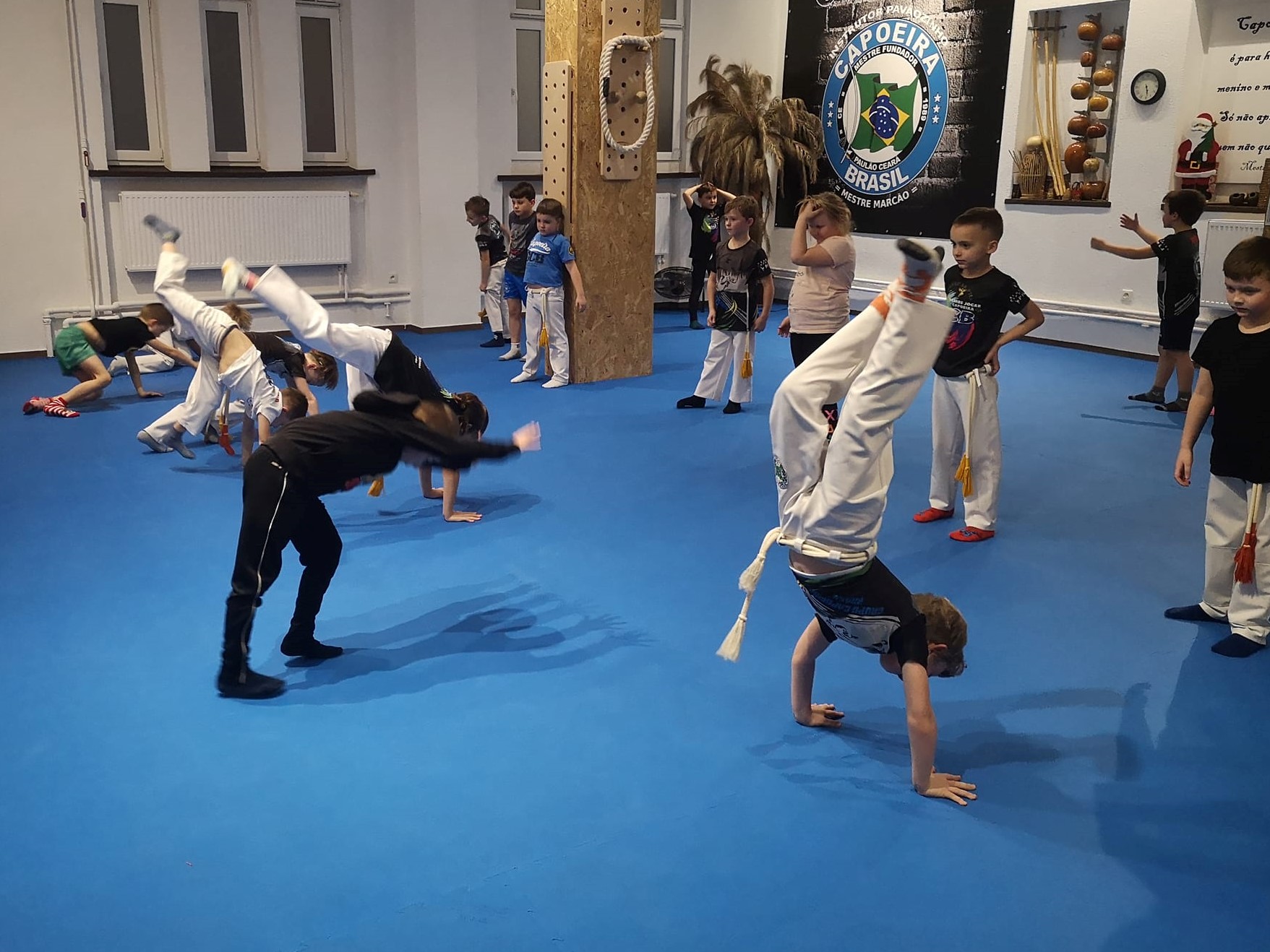  Dzieci w&nbsp;strojach sportowych wykonują ćwiczenia gimnastyczne w&nbsp;hali sportowej.
