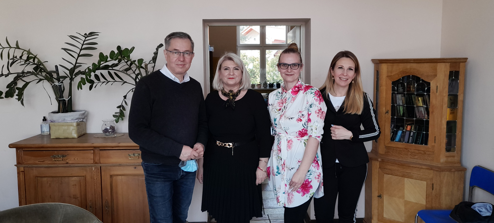 Pomieszczenie. Trzy kobiety i mężczyzna stoją. Meble biurowe.