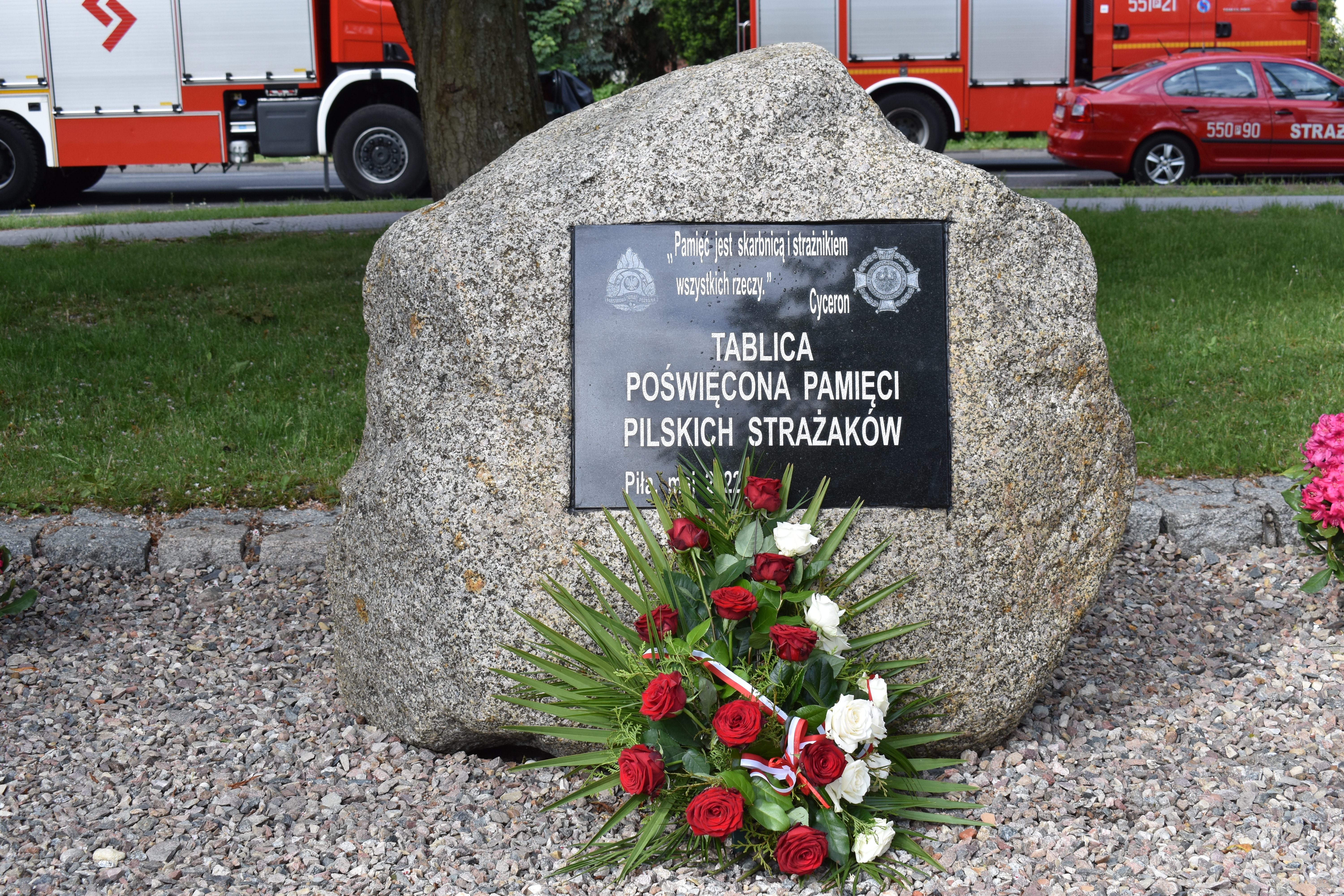 Głaz, obelisk, tablica pamiątkowa. Wiązanka kwiatów.