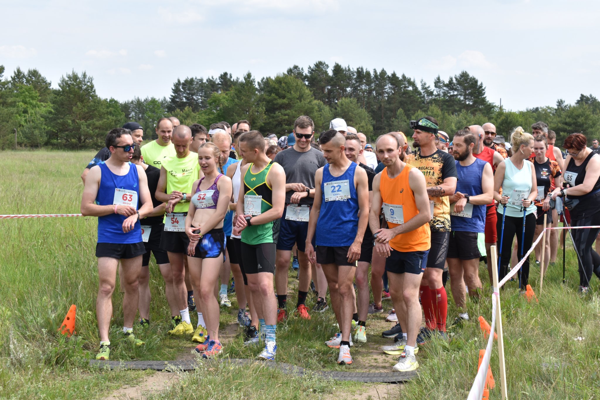 grupa zawodników stoi przed startem, czekają na uruchomienie zegarków, trzymają ręce na nadgarstkach.