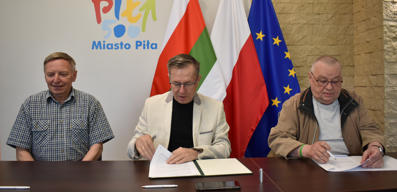 reprezentacyjne pomiszczenie. Trzech mężczyn podpisuje dokumenty.