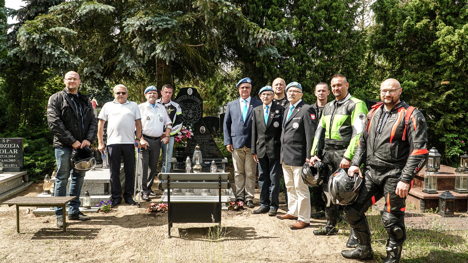 zdjęcie grupa mężczyzn- część w strojach motocyklowych, część z elementami niebieskimi (czapki, chusty) stoją przy grobie