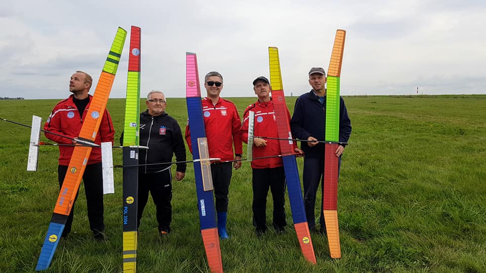 Zawodnik z Pilskiego Klubu Modelarzy Lotniczych w Mistrzostwach Świata Modeli Latających Pięciu mężczyzn na świeżym powietrzu, wokół duża przestrzeń. Każdy z mężczyzn trzyma w ręce model latający.