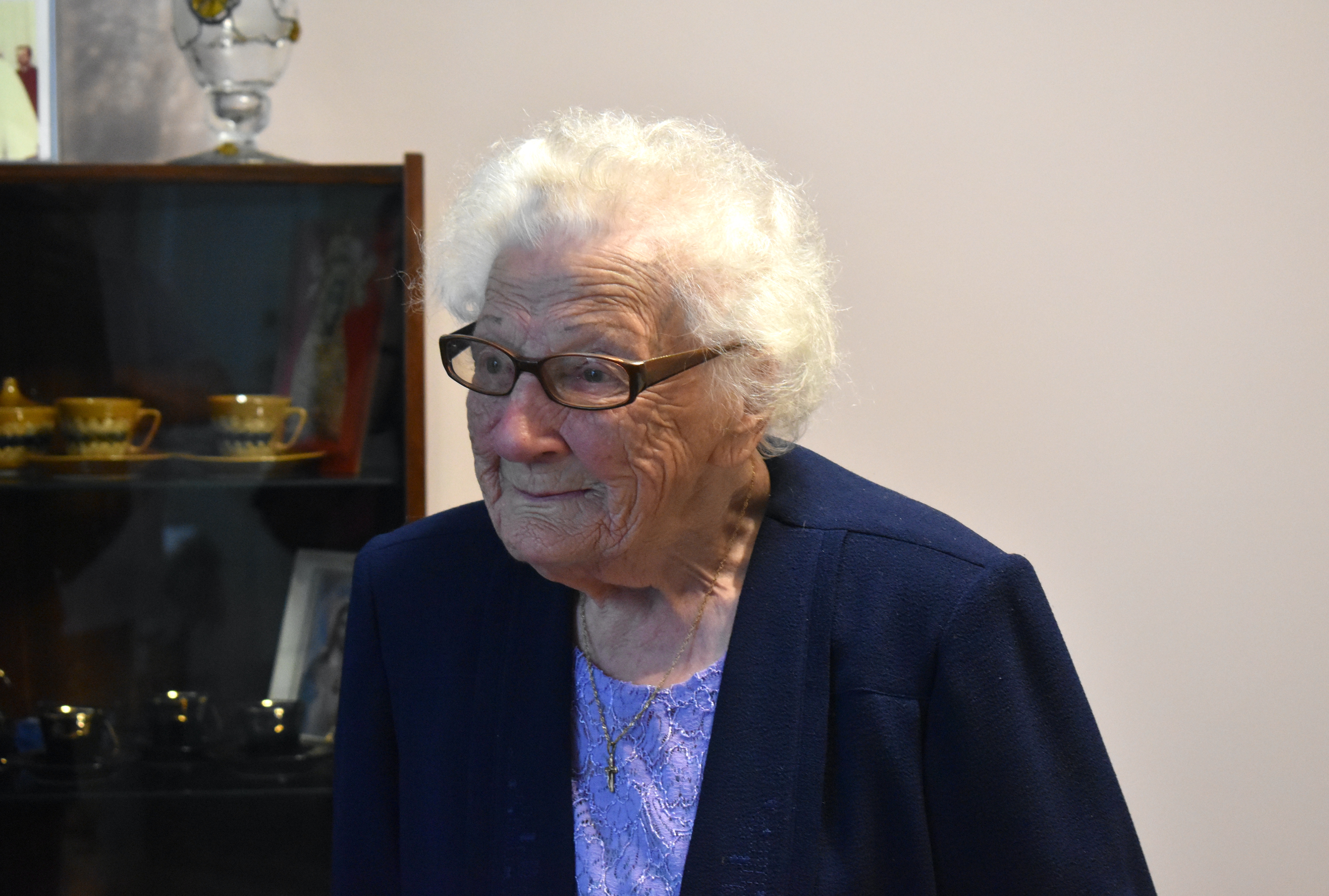 Portretowe zdjęcie starszej kobiety, ubranej odświętnie, uśmiechającej się.