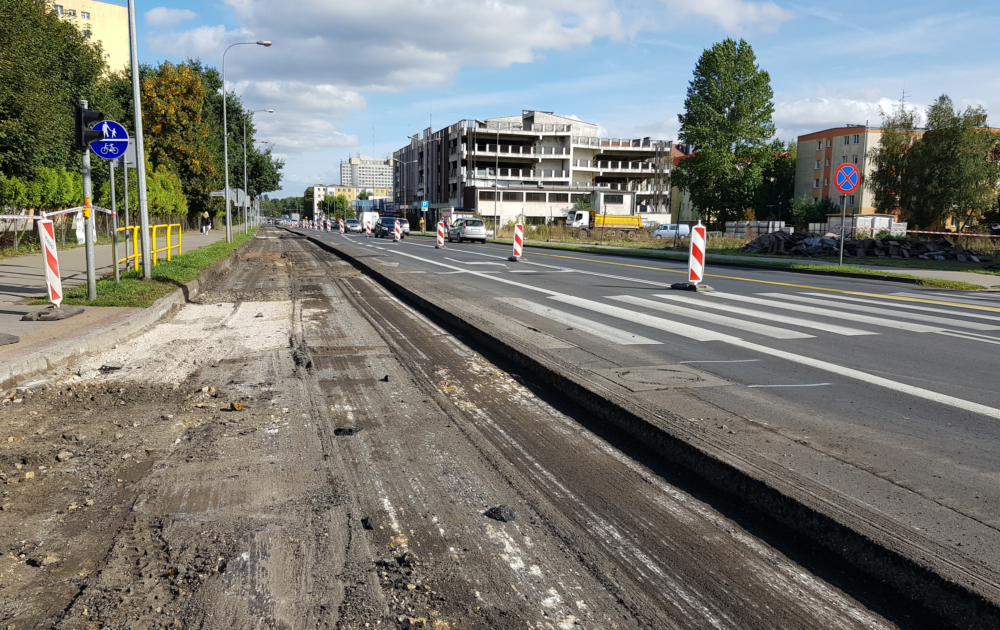 Ulica kilkupasmowa, po dwóch stanach zabudowania, znak informujący o&nbsp;chodniku i&nbsp;ścieżce dla rowerów. W tle zabudowania, drzewa i&nbsp;jadące ulicą auta. Po lewej stronie nawierzchnia jezdni całkowicie zdarta, w&nbsp;trakcie przebudowy.