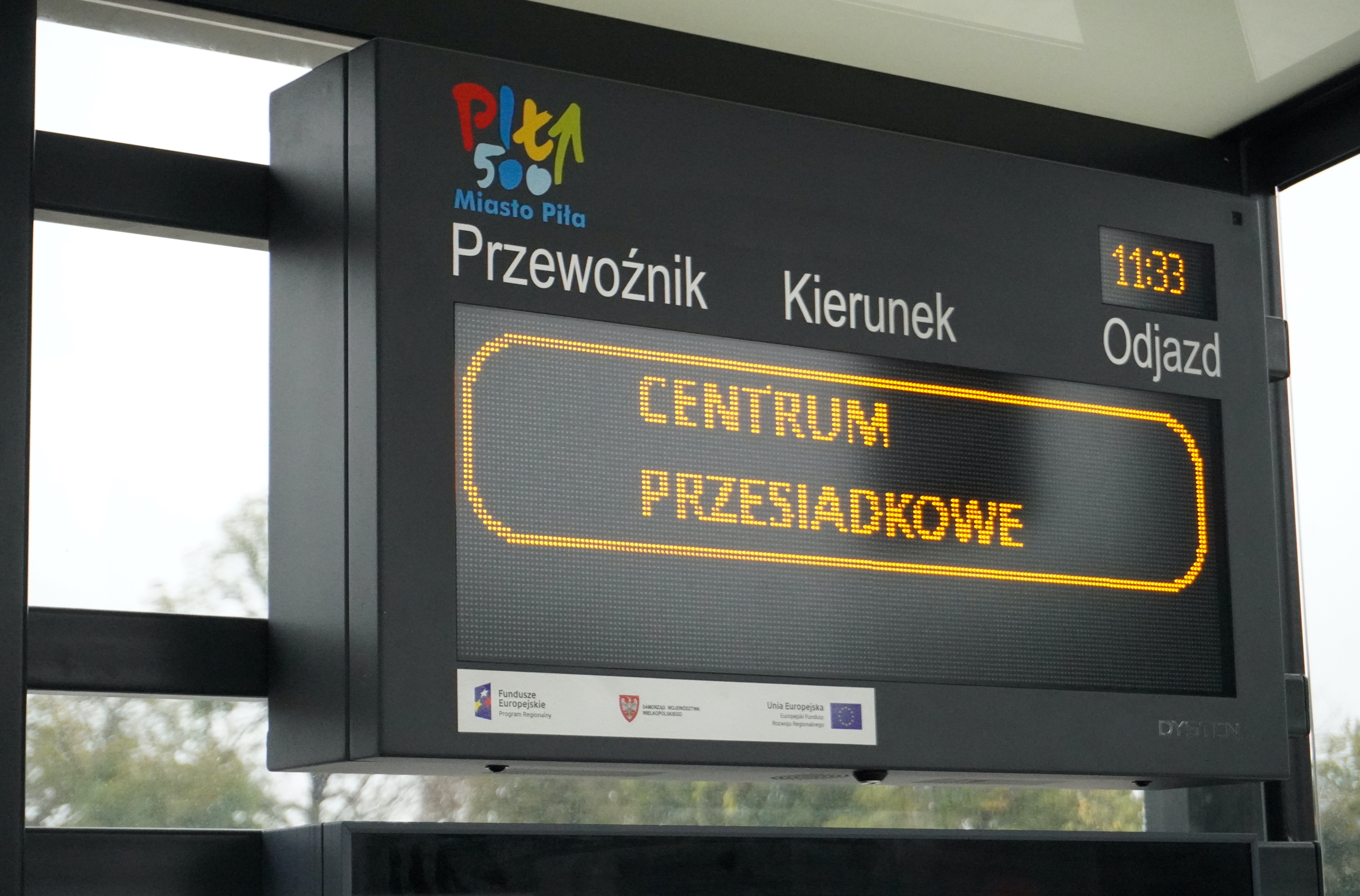 Tablica informacji pasażerskiej wyświetlająca napis: Centrum przesiadkowe. Logo Miasto Piła.