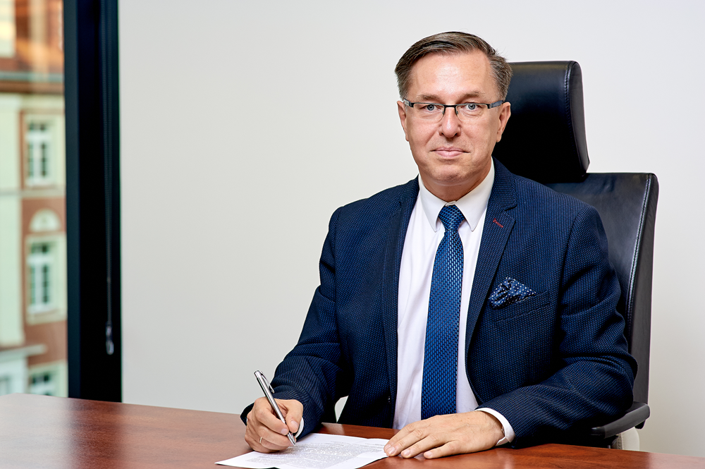 Mężczyzna siedzący przy biurku, na&nbsp;kt&oacute;rym leży pismo. W prawej dłoni długopis. Za prezydentem biała czysta ściana i&nbsp;w lewym narożniku duże okno.