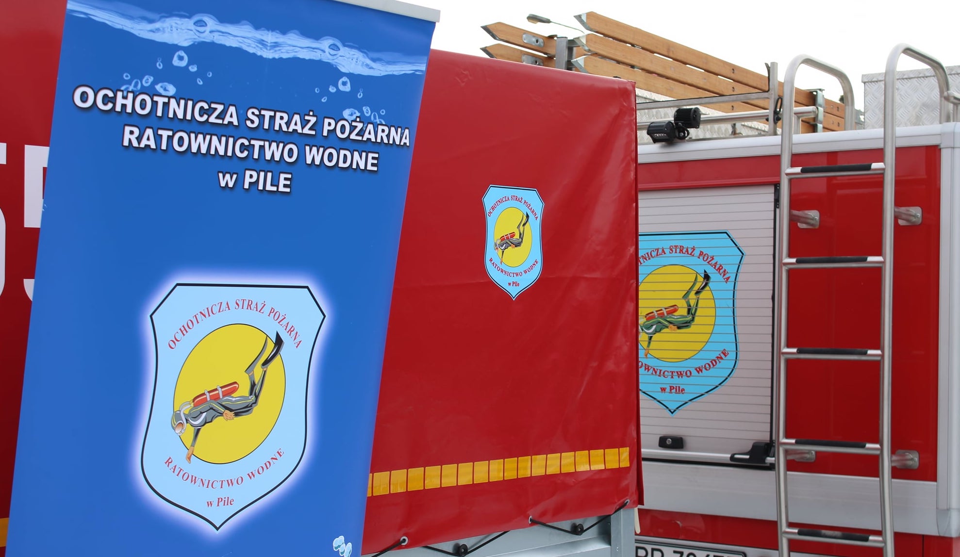 Nowy pojazd ratowniczo-gaśniczy dla OSP RW w Pile Wozy strażackie, roll up z napisem: Ochotnicza Straż Pożarna Ratownictwo Wodne w Pile.