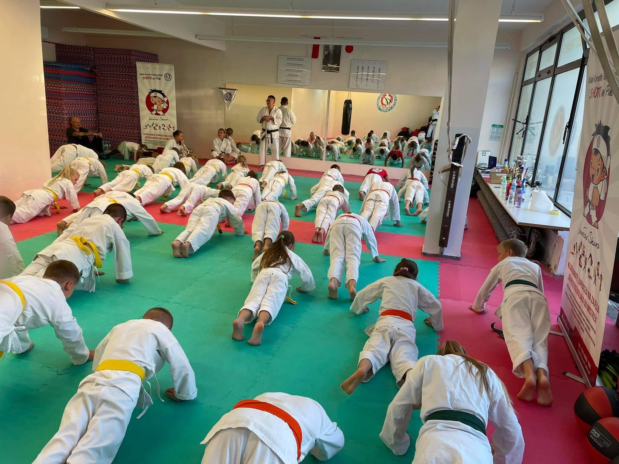 30 000 złotych dla KKT SHOTO! Dzieci w sali do ćwiczeń wykonują pompki na macie. Każdy ma na sobie kimono.