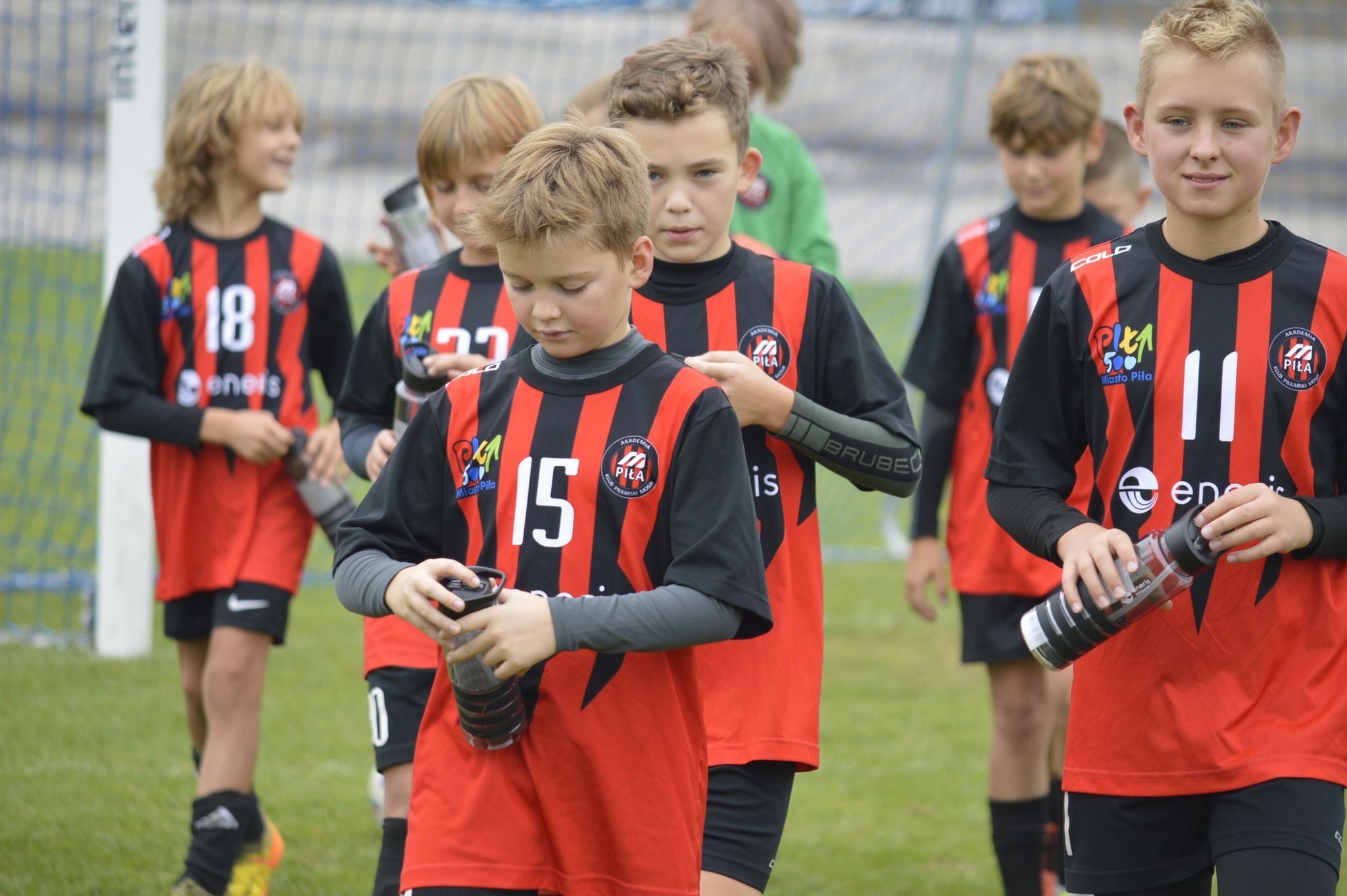Na boisku grupa chłopców w jednakowych czerwono-czarnych strojach sportowych z logo miasto piła i akademia klub piłkarski piła.