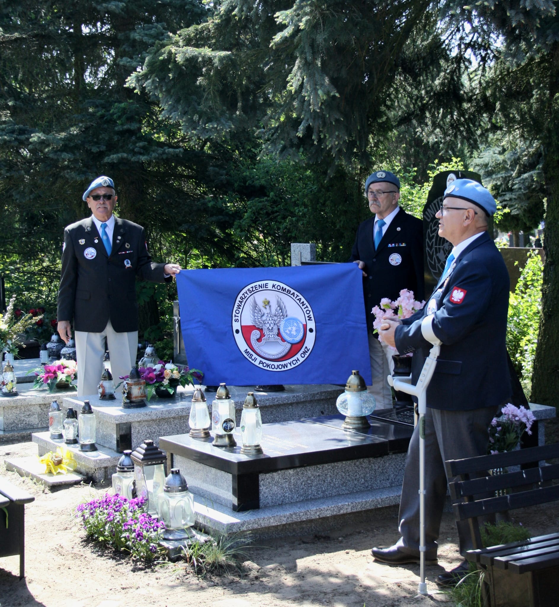 mężczyźni przy grobie trzymają niebieską flagę stowarzyszenia