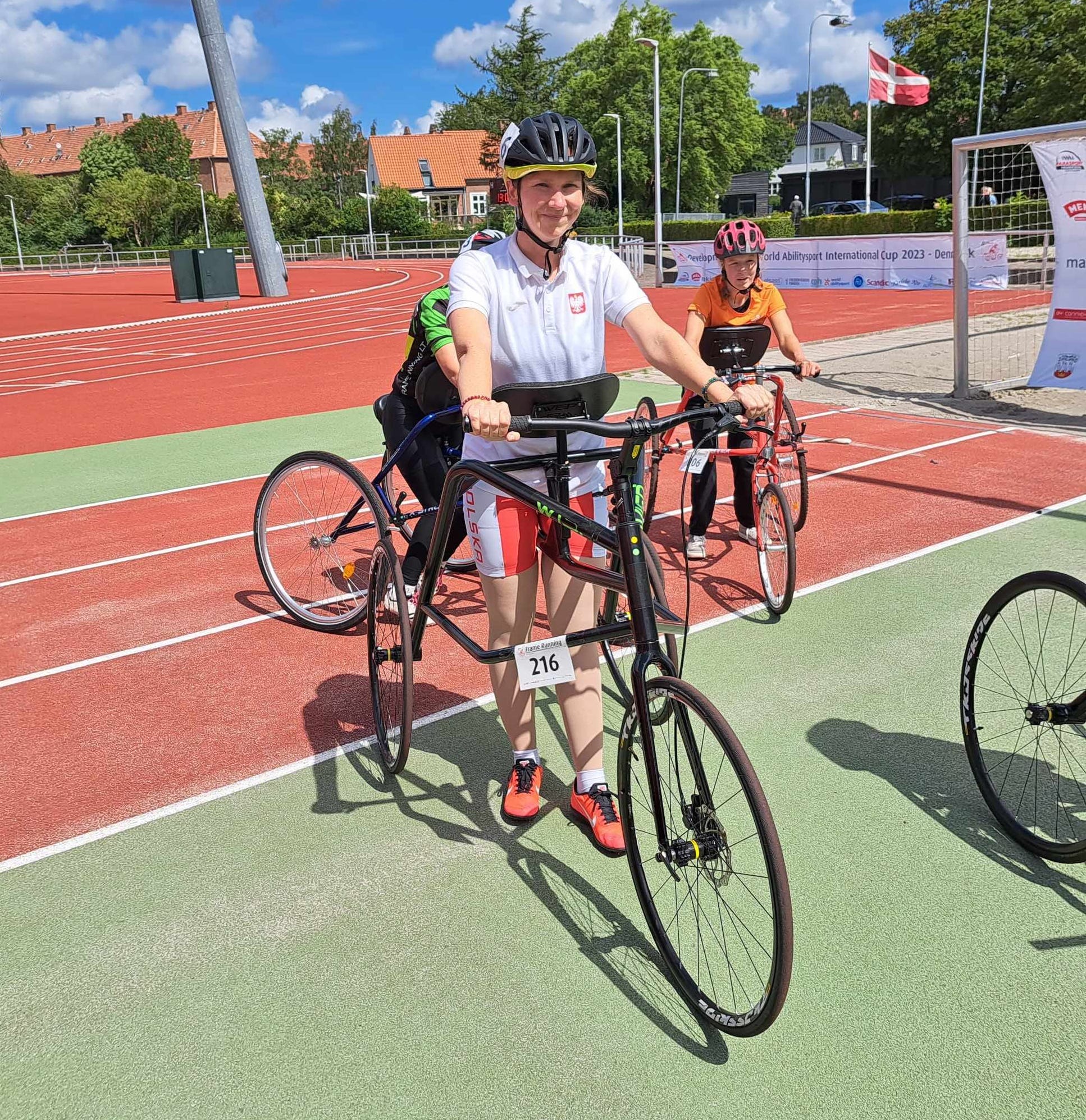 Frame Running | kolejne zawody - kolejne sukcesy Zawodnicy na stadionie, w sportowych strojach, na głowach mają kaski. Każdy stoi przy trójkołowym rowerze do Frame running.