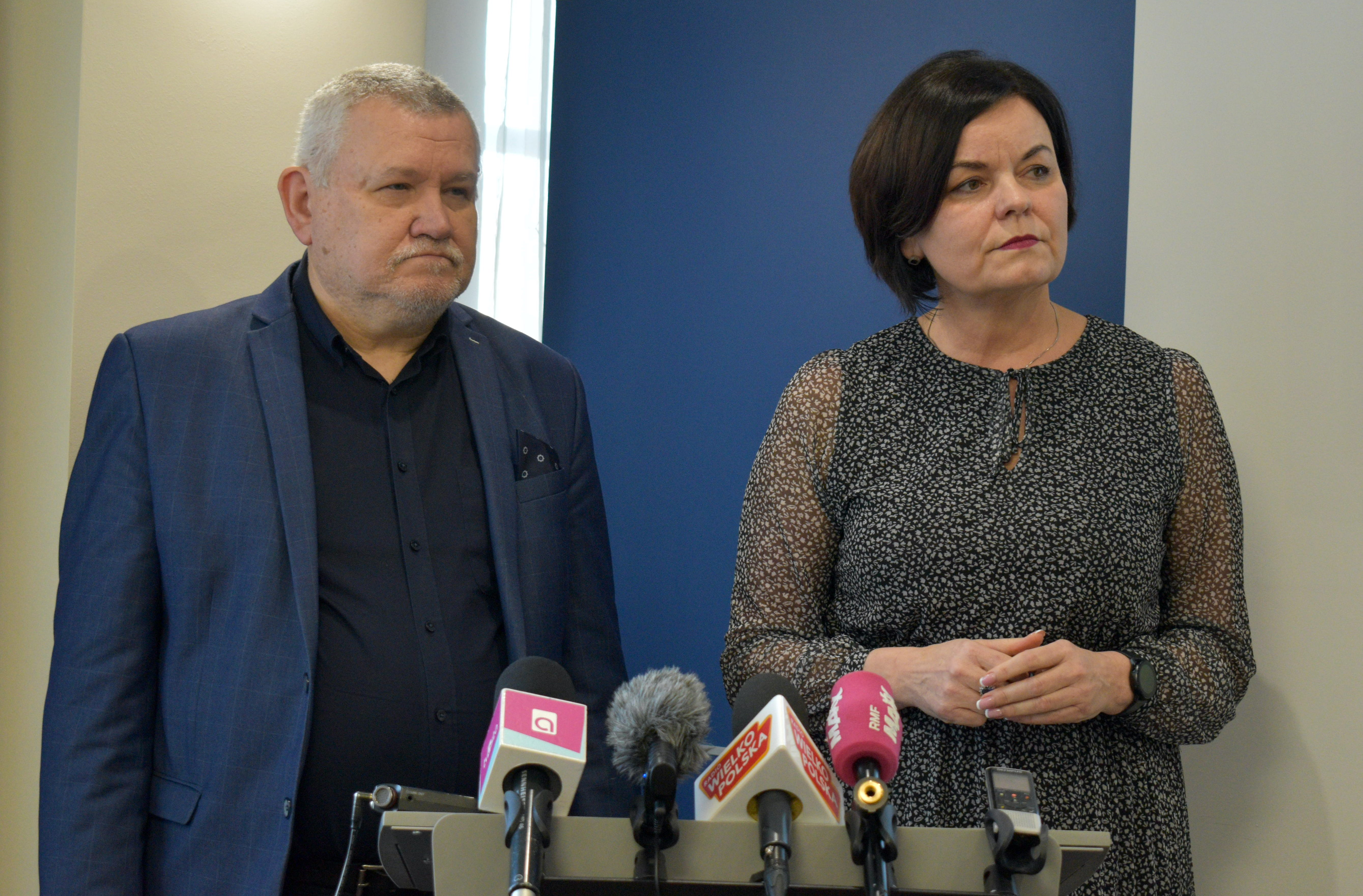 Kobieta i&nbsp;mężczyzna stojący przed m&oacute;wnicą, przy kt&oacute;rej widać mikrofony stacji radiowych i&nbsp;telewizyjnych.