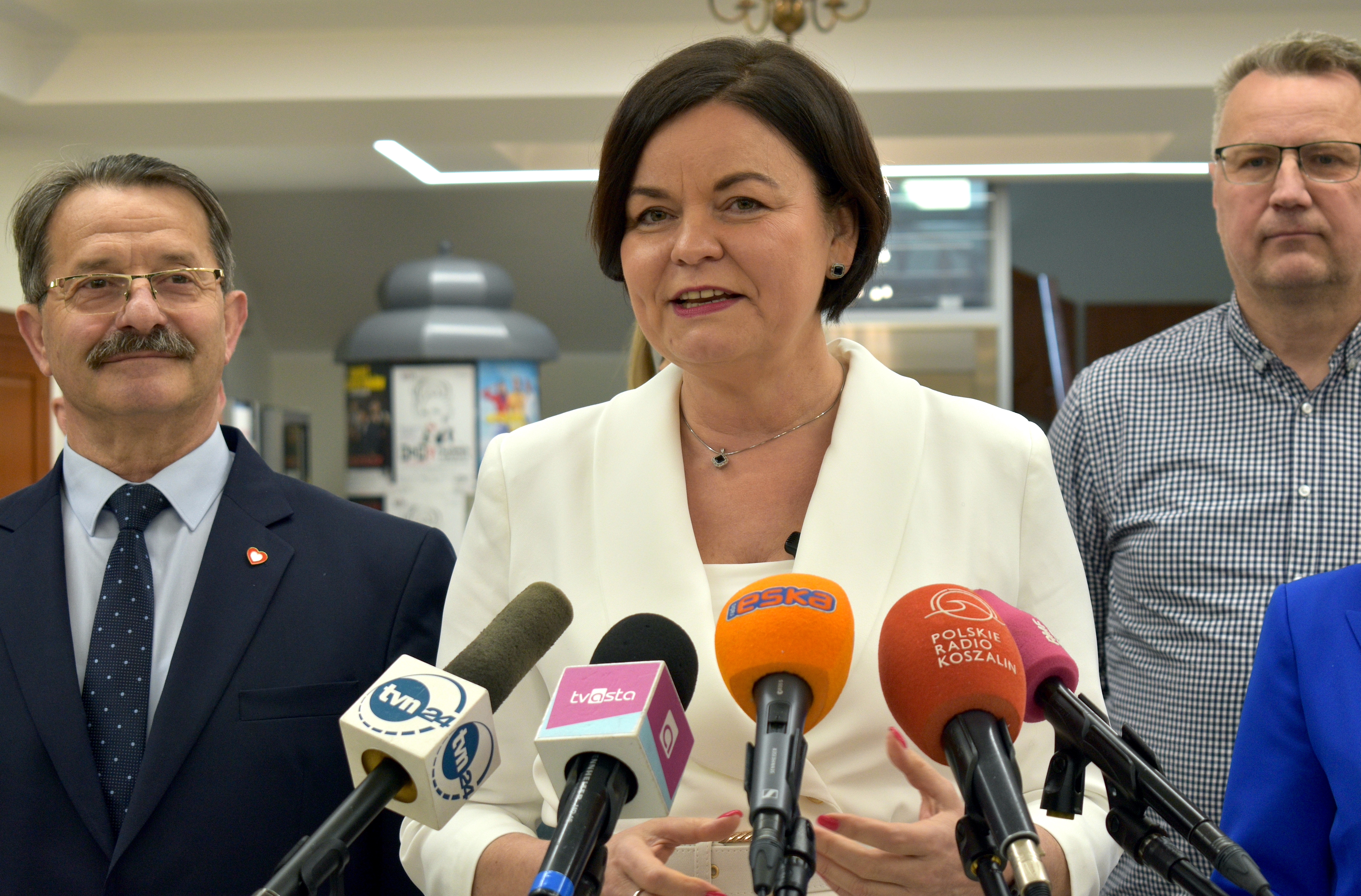 Kobieta przed mikrofonami stacji radiowych i&nbsp;telewizyjnych, obok niej i&nbsp;w tle mężczyźni i&nbsp;kobieta.