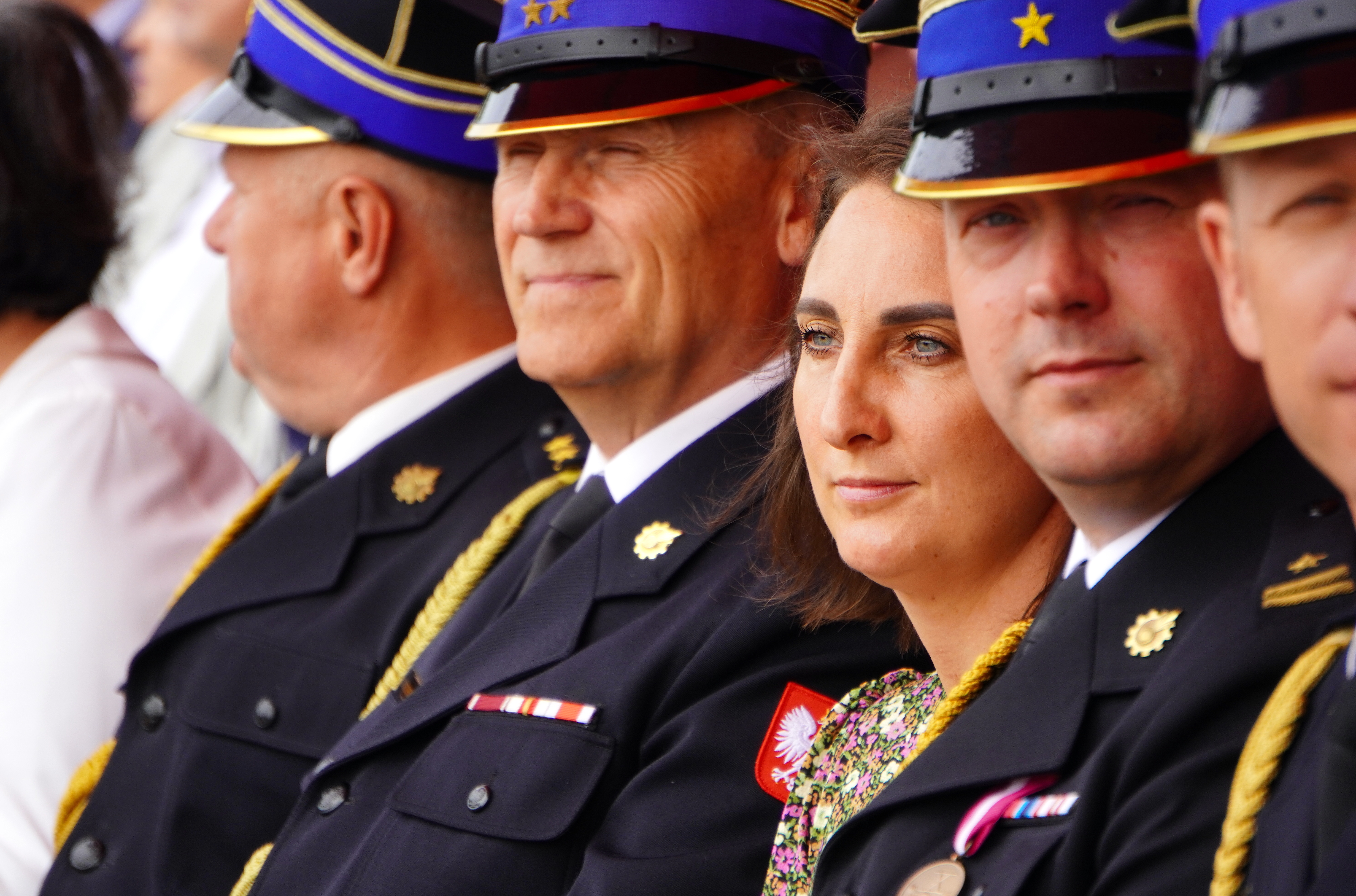 Mężczyźni w&nbsp;strażackich mundurach, wśr&oacute;d nich kobieta w&nbsp;kwiecistej sukience.
