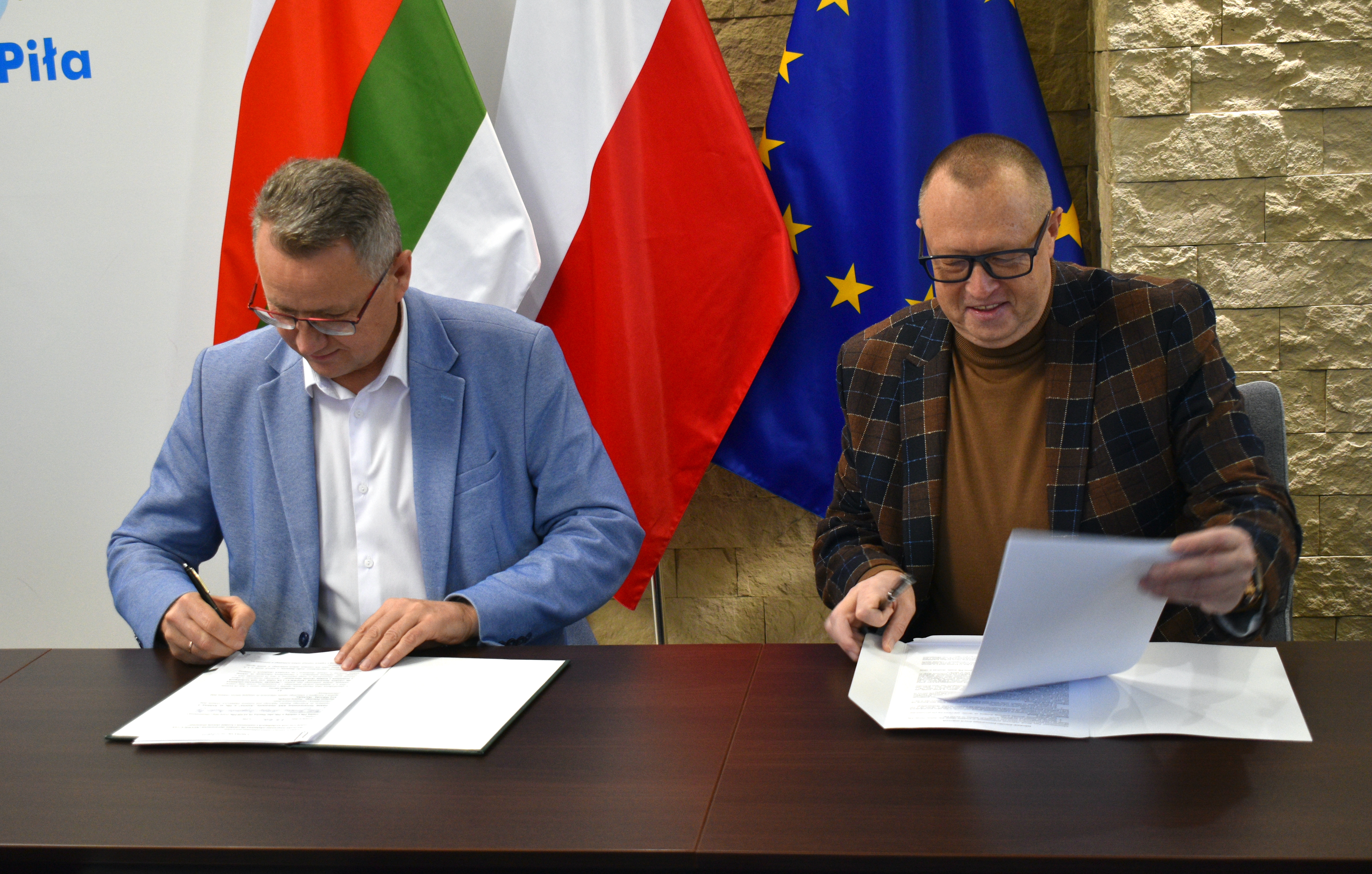 Dw&oacute;ch mężczyzn podpisujących umowy przy stole 