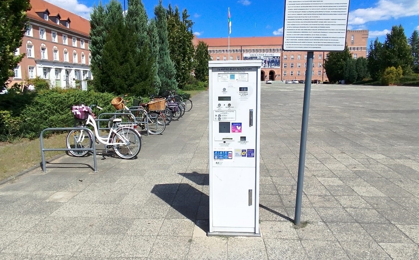 Parkomat na&nbsp;placu, obok stojaki i&nbsp;przypięte do nich rowery