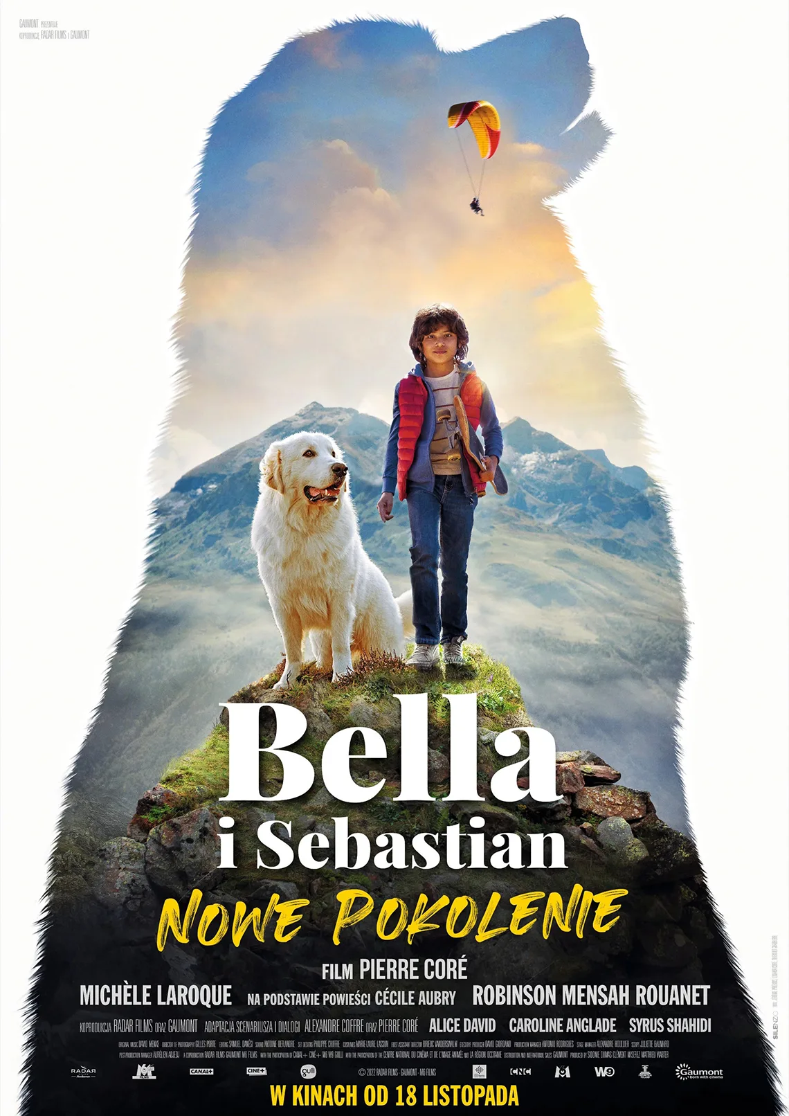 Bella i Sebastian: Nowe Pokolenie Chłopiec z białym dużym psem stoją na szczycie góry. Zdjęcie w kształcie psa. Treść: Bella i Sebastian nowe pokolenie.
